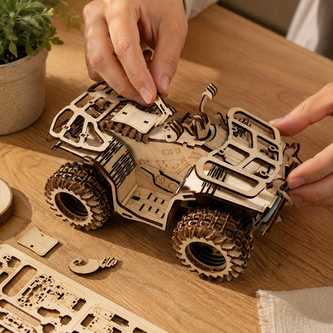 Hands assembling the wooden ATV puzzle on a workbench.