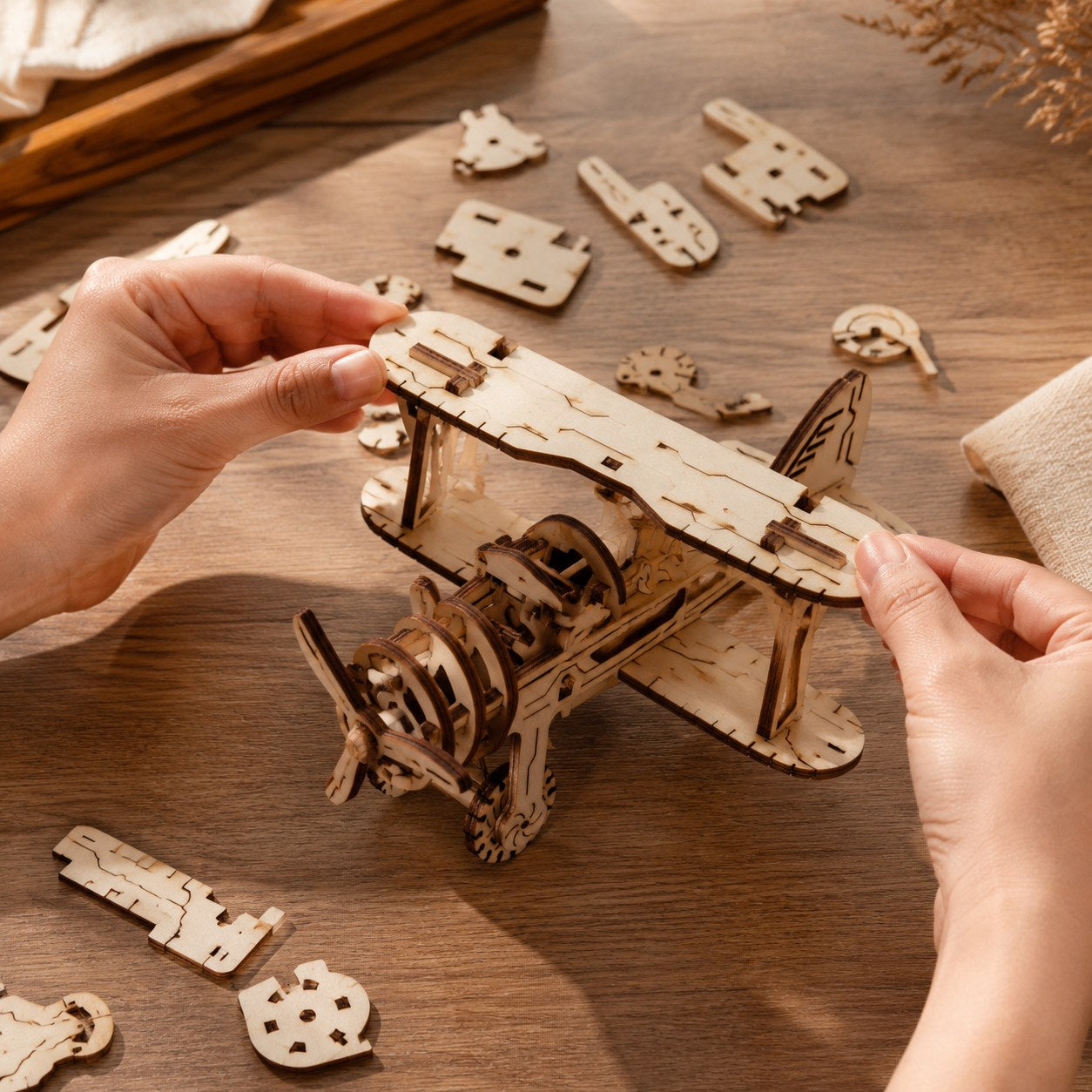 Adult hands assembling the wooden biplane model on a workbench