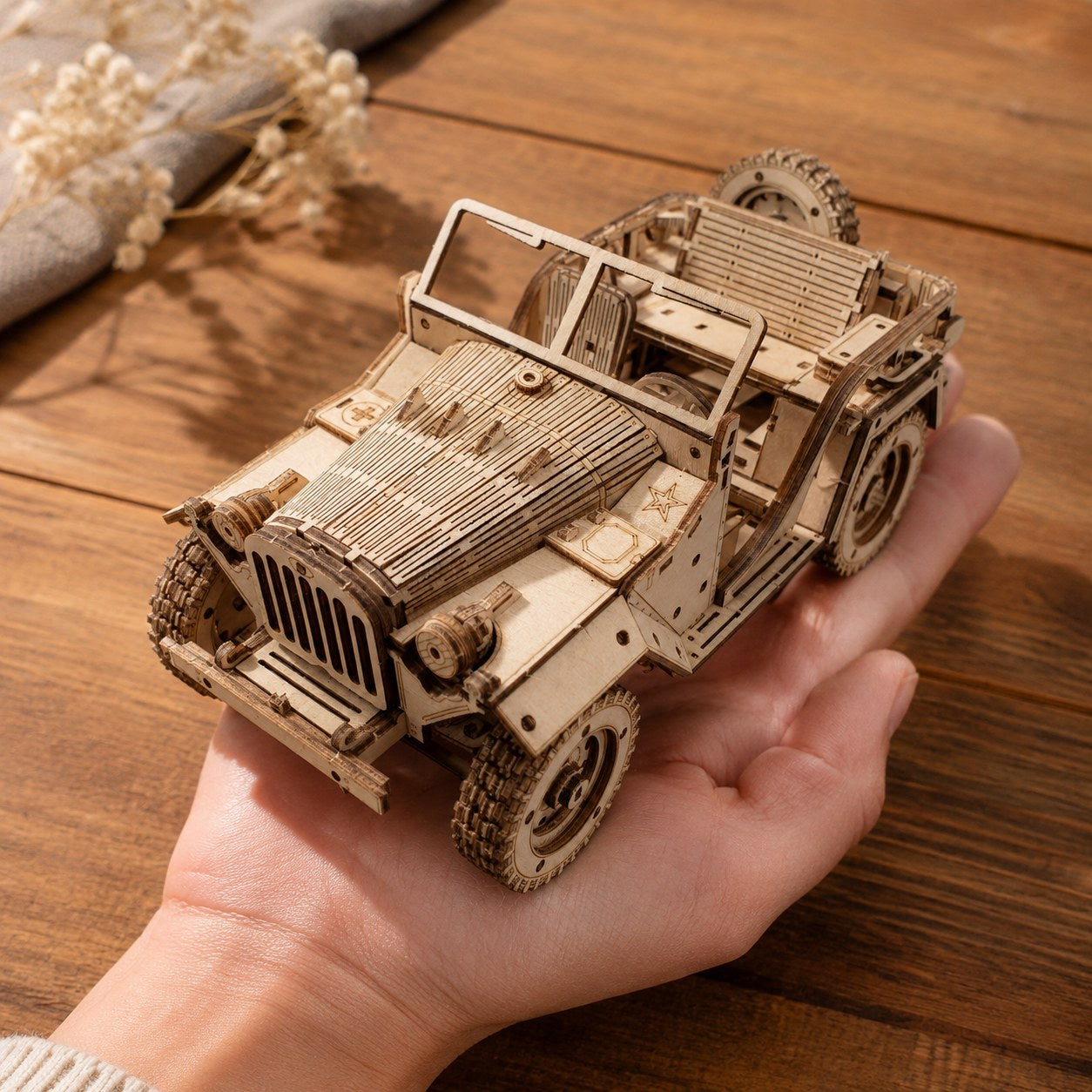 Adult hand holding the assembled vintage off-road vehicle wooden puzzle to show scale.