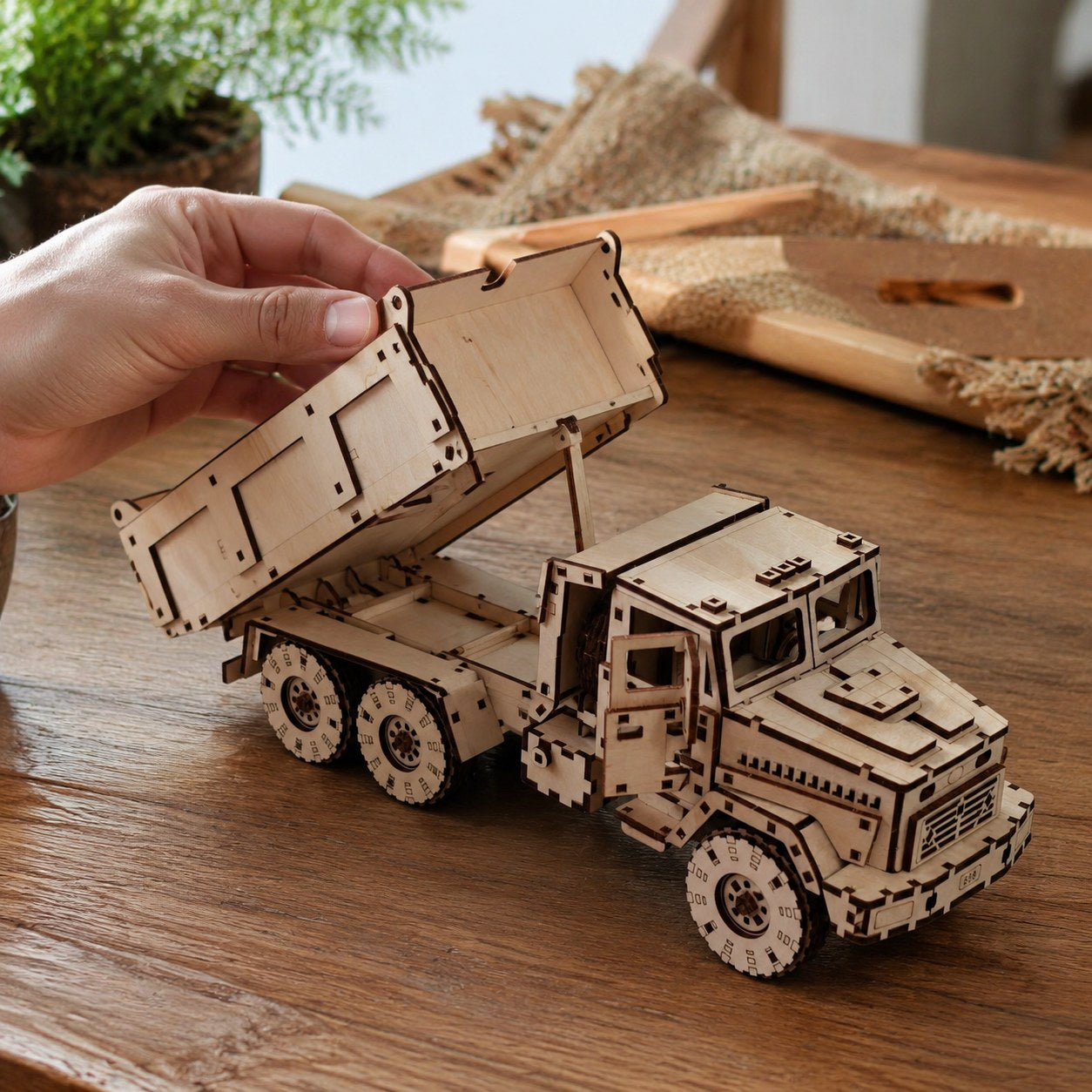 Adult hand tilting the bed of the wooden dump truck model to show scale
