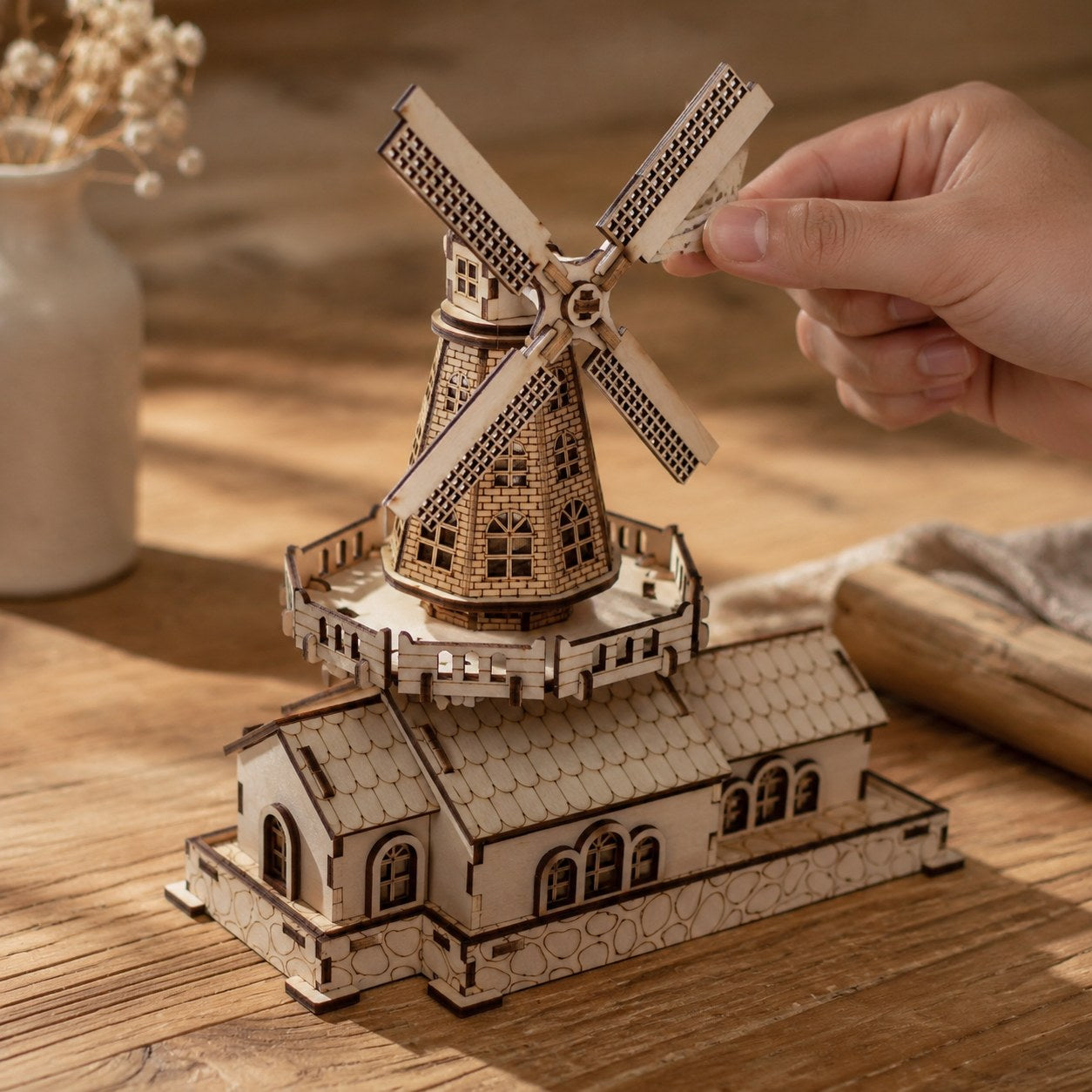 Adult hand adjusting the rotor of a wooden windmill model to show scale