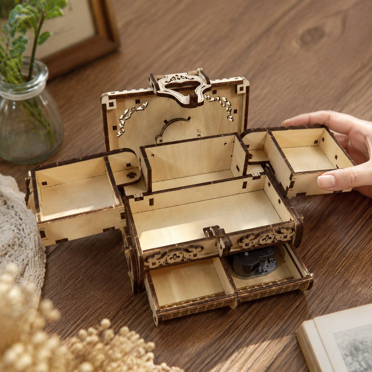 Hand opening the expanding trays of the wooden jewelry box to show scale