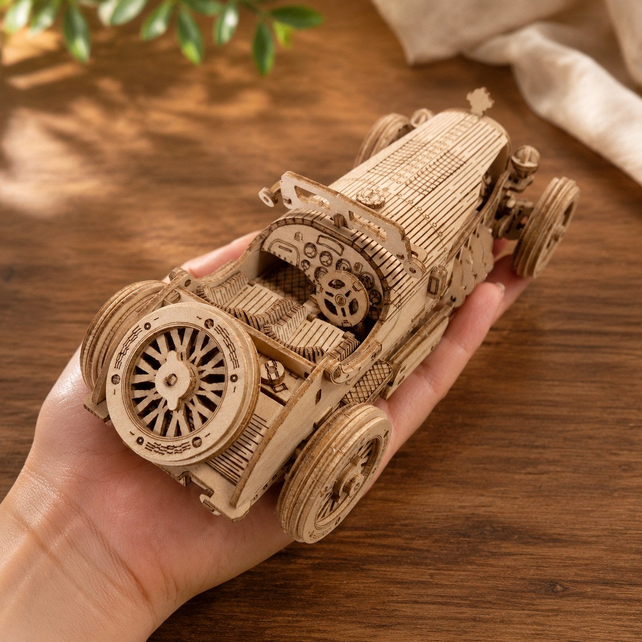 Adult hand holding the finished vintage sports car wooden model to show scale.
