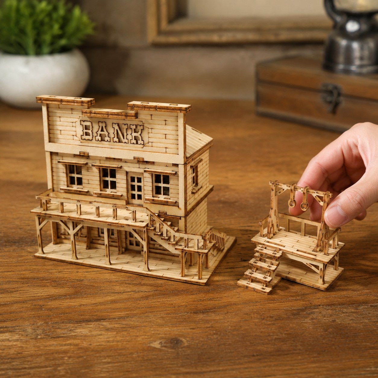 Hand placing the wooden gallows next to the bank model for scale