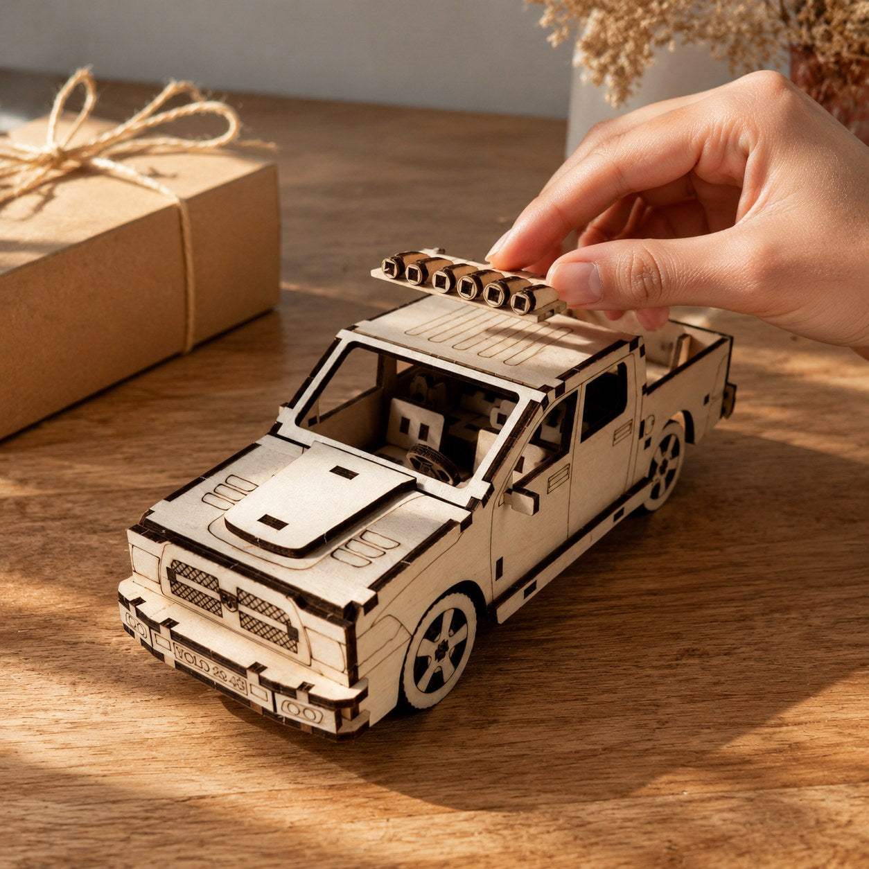 Hand adjusting the roof light bar on a wooden pickup truck model to show scale