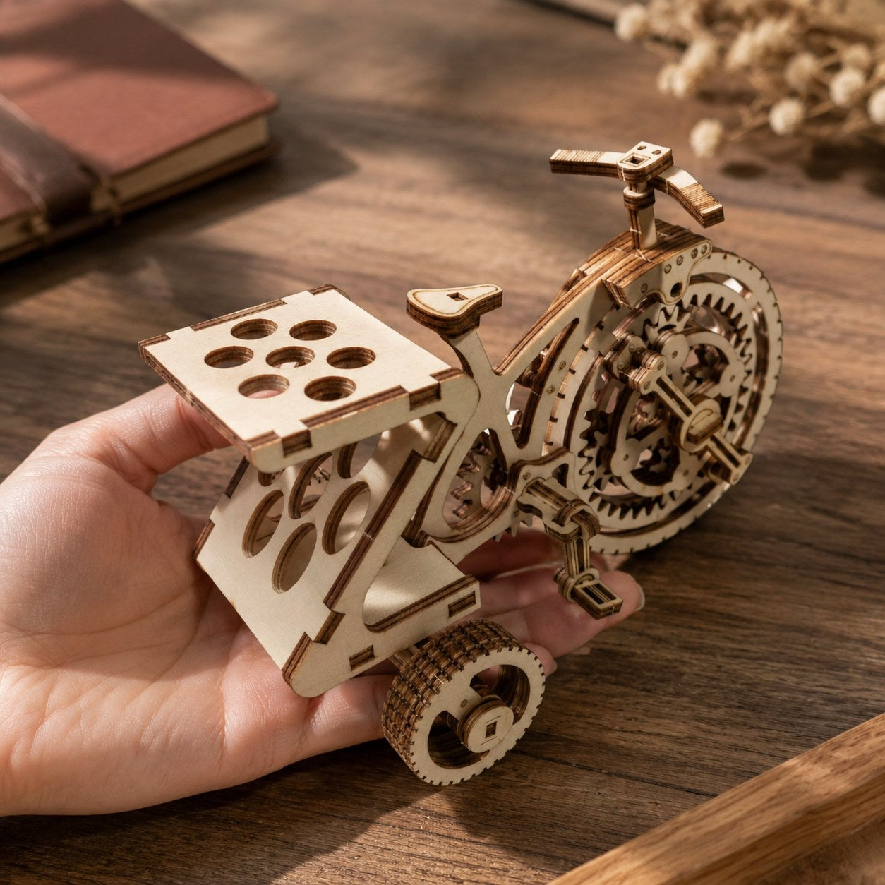 Adult hand holding the assembled wooden tricycle model for scale