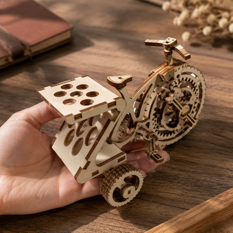 Adult hand holding the assembled wooden tricycle model for scale