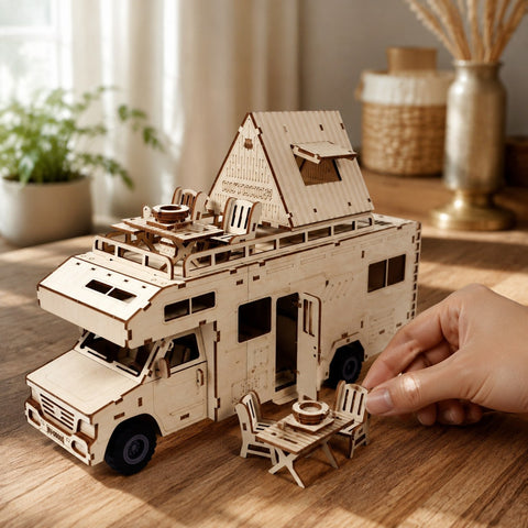 Adult hand placing miniature wooden camping furniture next to the RV model to show scale