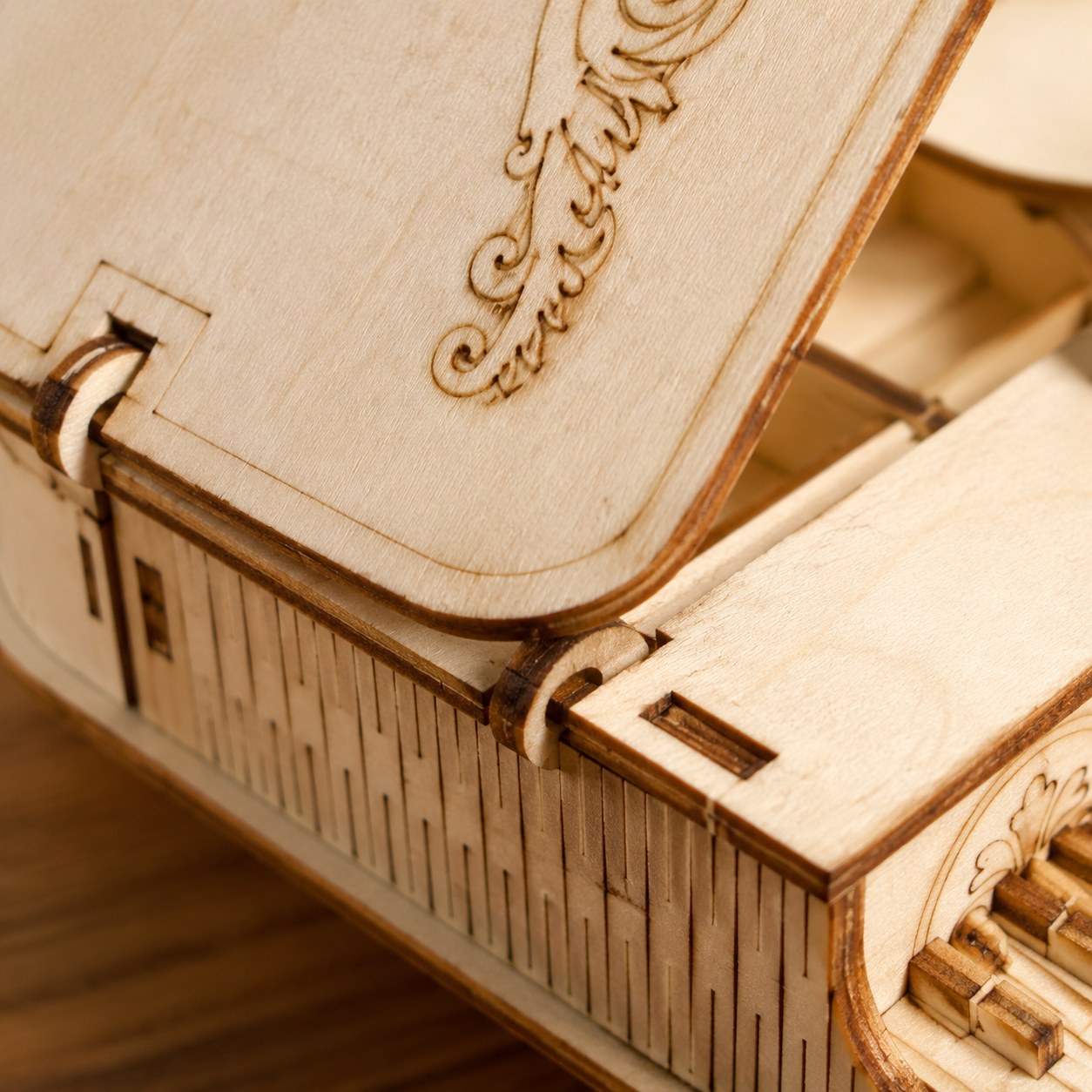 Macro close-up of the laser-cut engraved scrollwork and living hinge on the wooden piano